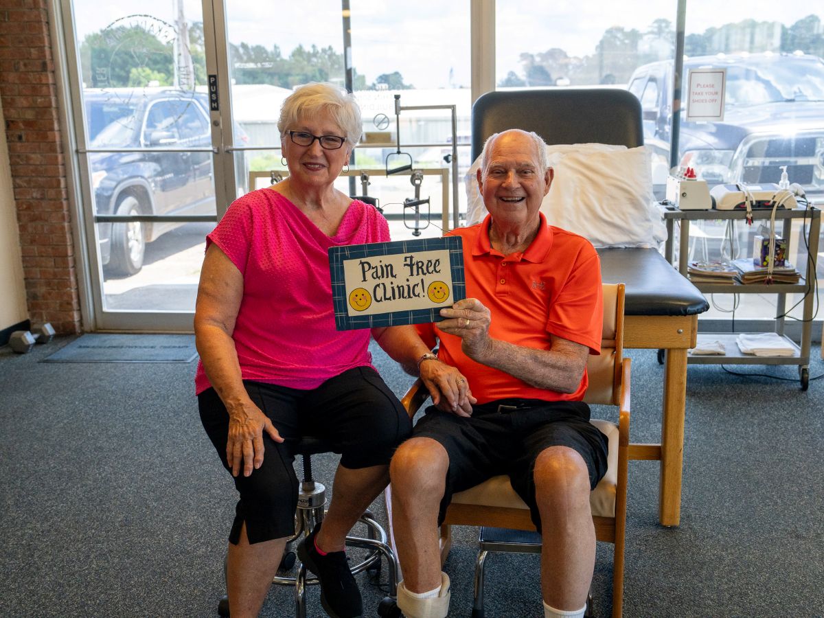 Happy senior couple posing with 'Pain Free Clinic' sign