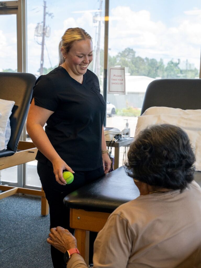 Therapist holding a tennis ball while engaging with senior patient
